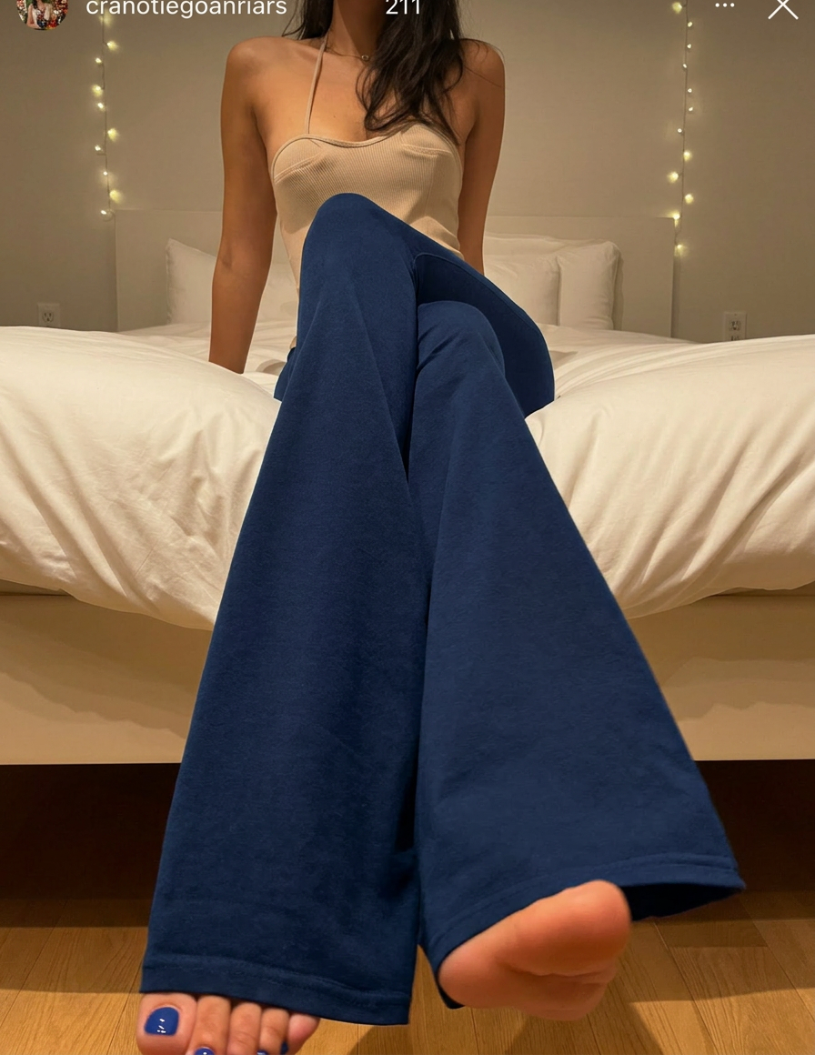 Cliente sentada na cama usando a calça Noir azul marinho, mostrando a abertura flare e o caimento do tecido.
