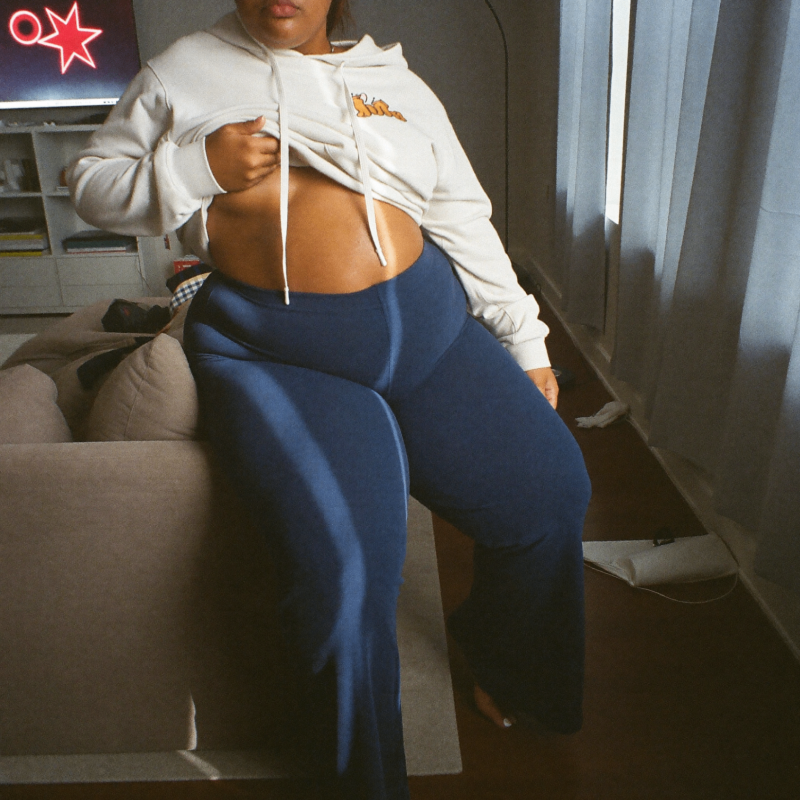 Cliente apoiada no sofá usando a calça Noir azul marinho com cropped bege, mostrando o caimento na cintura e quadril.